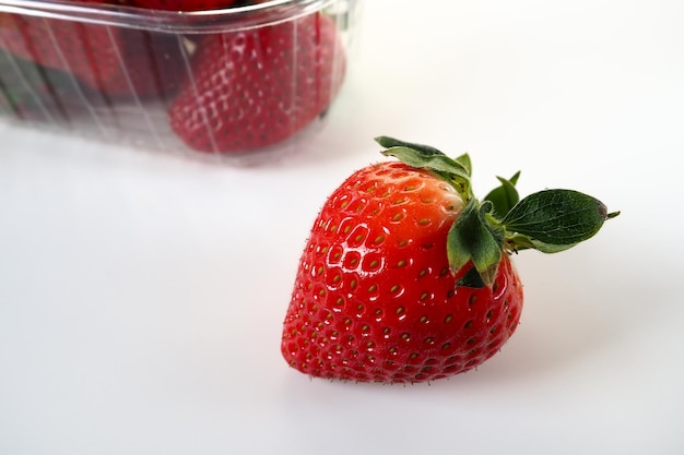 Rijpe aardbeien in een plastic verpakking op een witte achtergrond Heerlijke verse bessen in een container te koop aan klanten Voedsel vers houden Gezonde voeding Een aardbei uit de container getrokken