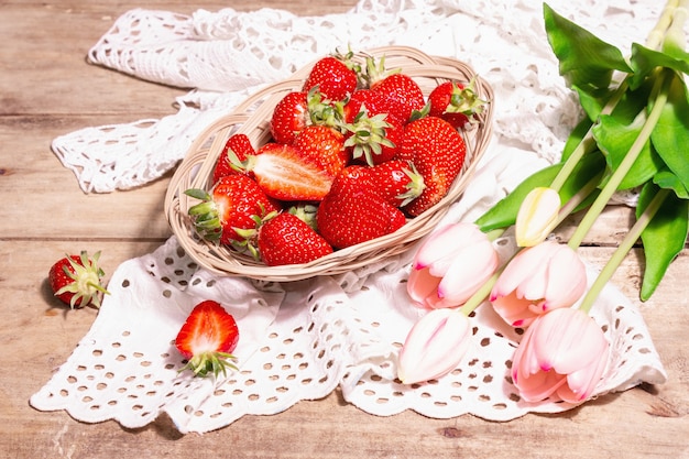 Rijpe aardbeien in rieten plaat. Verse bessen, aromatische munt, roze tulpen. Oude houten tafel, vintage gehaakt servet, rustieke stijl, kopieer ruimte