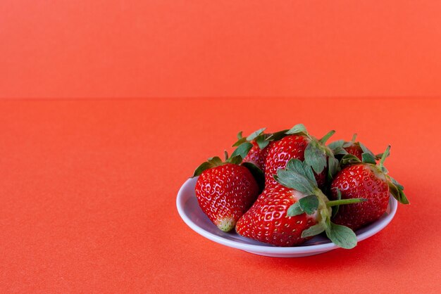 Rijpe aardbeien op een bord op een rode achtergrond, kopieer ruimte