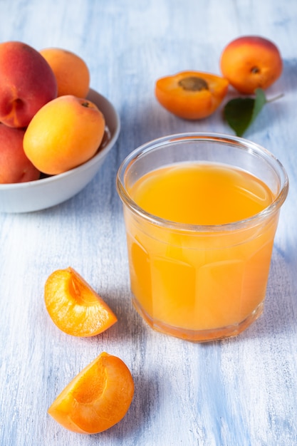 Rijpe abrikozen en glas abrikozensap op blauwe rustieke muur met exemplaarruimte. Selectieve aandacht. Eco food concept. Frisse zomerdrankjes. Detox. Niet alcoholisch. Verticaal