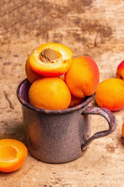 Rijpe abrikozen in een vintage ijzeren mok. Zoet fruit, oude houten tafel, close-up