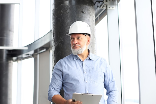 Rijpe architect die veiligheidshelm draagt die nieuw gebouw inspecteert.