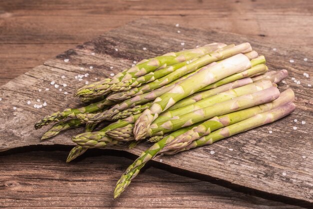 Rijpe asperges klaar om te koken. Vintage houten stands, hard licht, donkere schaduw. Oude planken achtergrond, kopieer ruimte