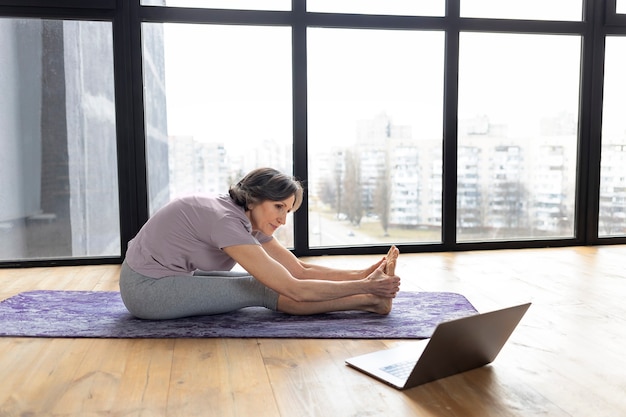 Foto rijpe atletische vrouw die thuis yoga online doet