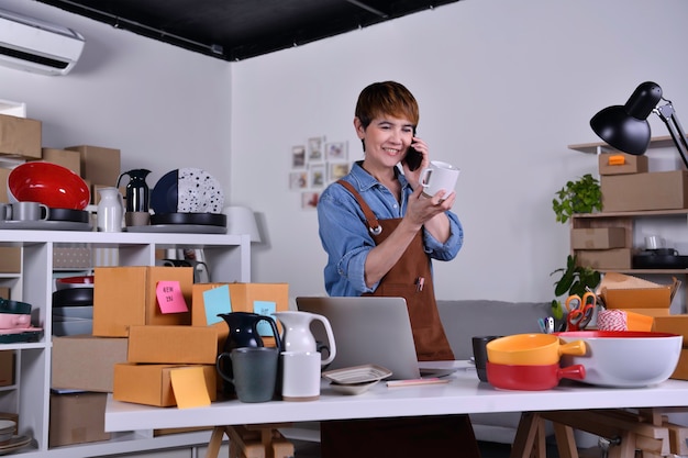 Rijpe Aziatische vrouwelijke ondernemer, bedrijfseigenaar die product controleert en aan de telefoon praat met de klant. Online verkoop zakelijk werk thuis concept