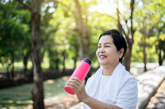 Rijpe Aziatische vrouwen die water drinken na een pauze die in de natuur traint, concept voor een gezonde oudere vrouw