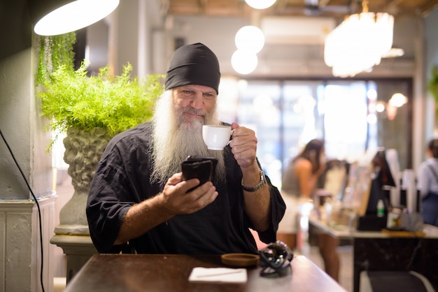 Rijpe bebaarde hipster man koffie drinken en het gebruik van telefoon in de coffeeshop