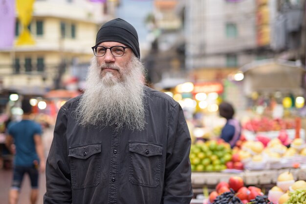 Rijpe bebaarde toeristische man met bril denken in Chinatown