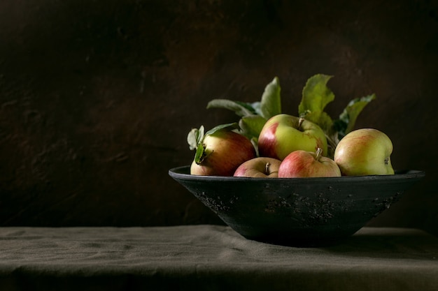 Rijpe biologische tuinieren groene rode appels met bladeren in grote keramische schotel staande op donkere tafelkleed. Zwarte achtergrond. Herfst oogst.