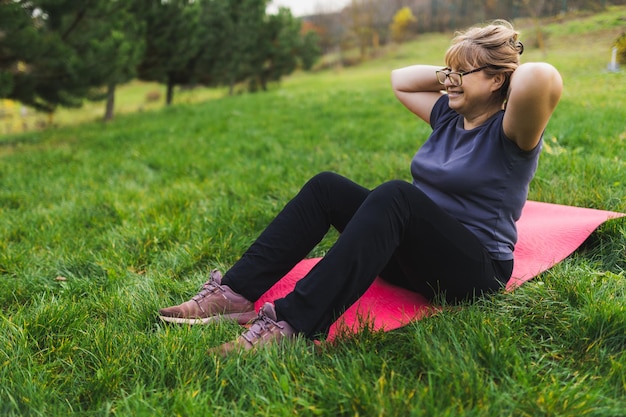 Rijpe blanke gepensioneerde vrouw in het park mediteert en voert ademhalingsoefeningen uit op zomerdag