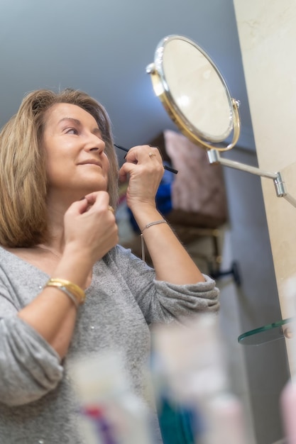 Rijpe blanke vrouw die schoonheidsbehandelingen toepast voor de spiegel van haar badkamer