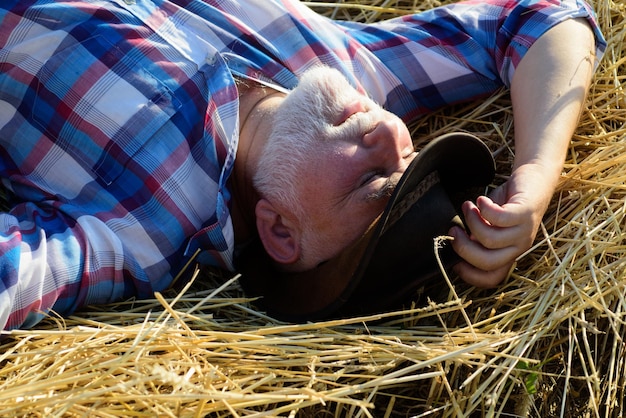 Rijpe boer in het hooi senior die een pauze neemt en ontspant op een hooi op een zomerdag grootvader la