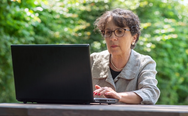 Rijpe brunette die laptop in de tuin met behulp van