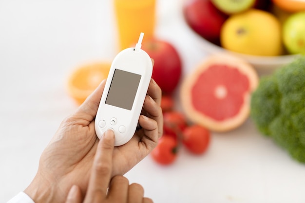 Rijpe europese vrouwelijke dokter voedingsdeskundige toont glucometer aan tafel met biologisch fruit en