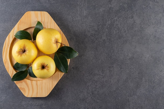 Rijpe gele appels met groene bladeren op houten plaat.