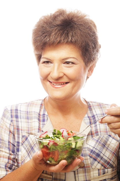 Rijpe glimlachende vrouw die salade eet