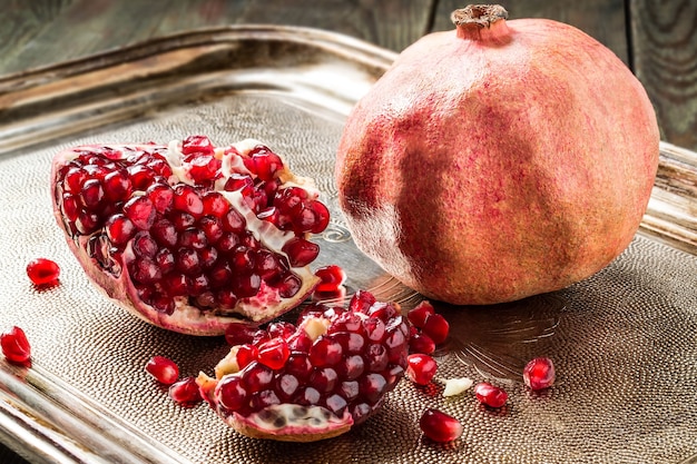 Rijpe granaatappel en stukjes met granen op metalen dienblad