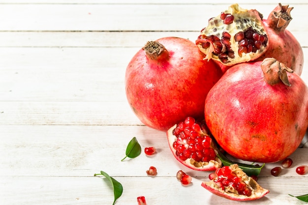 Rijpe granaatappels met bladeren. Op een witte houten tafel.