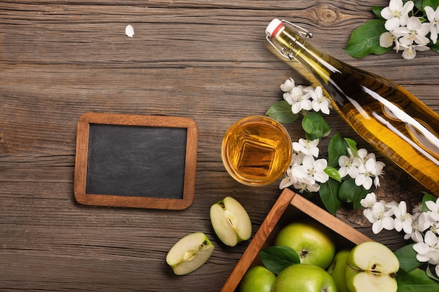 Rijpe groene appels in houten kist met tak van witte bloemen, glas, fles vers sap en krijtbord op een houten tafel. Bovenaanzicht met ruimte voor uw tekst.