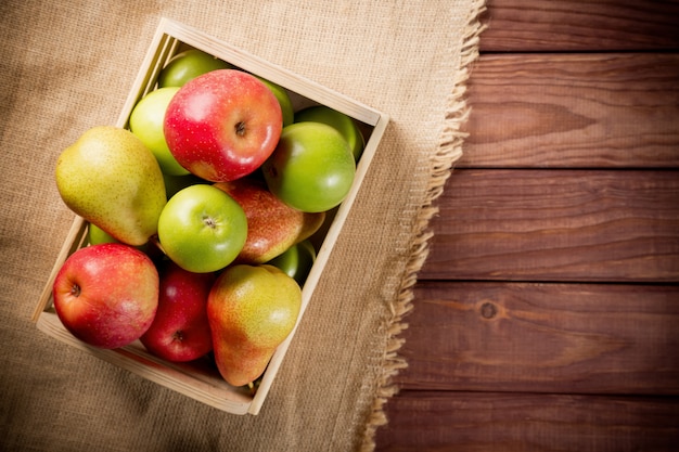 Rijpe groene en rode appels met peren in een houten doos