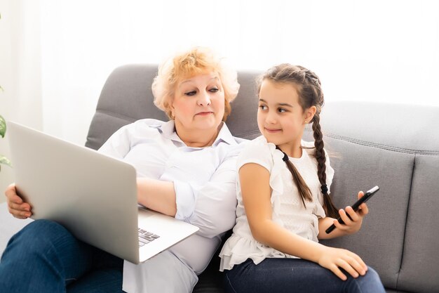 Rijpe grootmoeder helpt kind thuis met huiswerk. Tevreden oude oma helpt haar kleindochter met studeren in de woonkamer. Klein meisje schrijft op notitieboekje met senior leraar naast haar