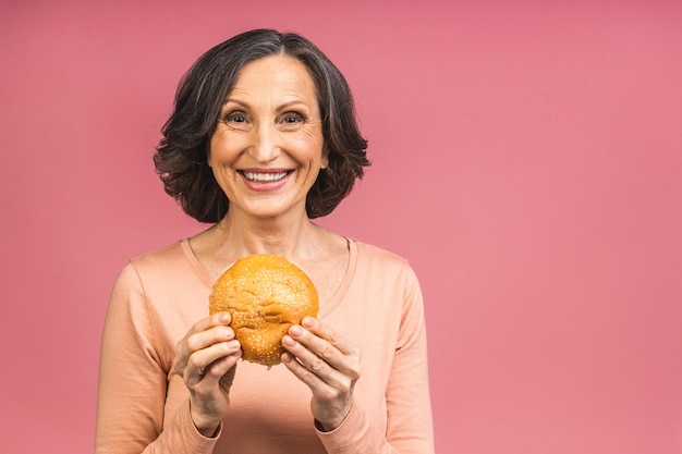 Rijpe hogere vrouw die hamburger met tevredenheid eet