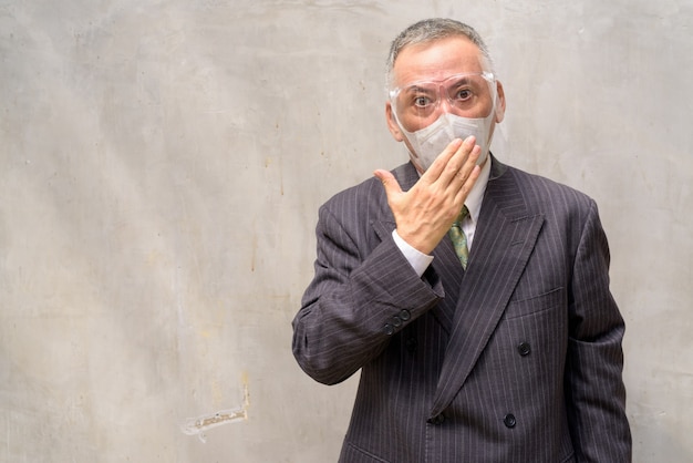 Rijpe Japanse zakenman die met masker en gezichtsschild geschokt kijkt