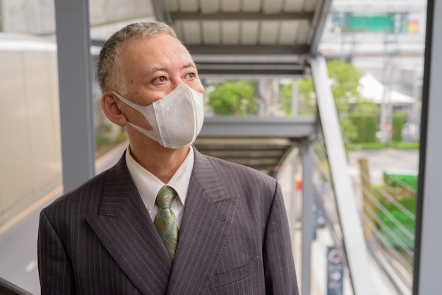 Rijpe japanse zakenman die met masker terwijl het gaan de treden in de stad denken