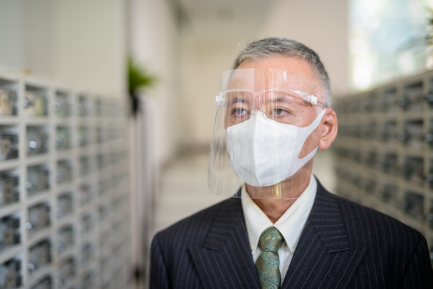 Rijpe japanse zakenman met masker en gezichtsschild bij de brievenbus