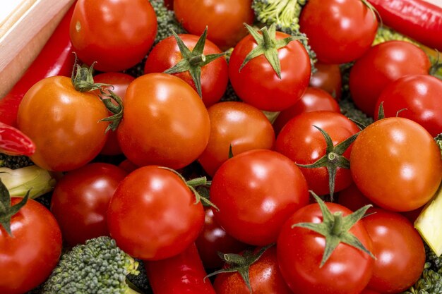 Rijpe kerstomaatjes in bulk gesneden van de tak en vergezeld van stukjes broccoli en hete rode chilipepers