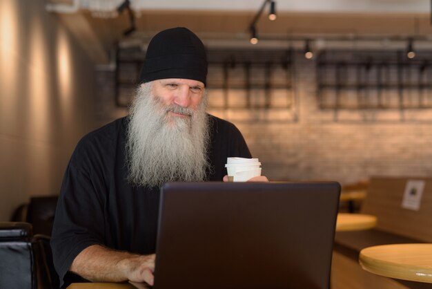 Rijpe knappe bebaarde hipster man met laptop in de coffeeshop