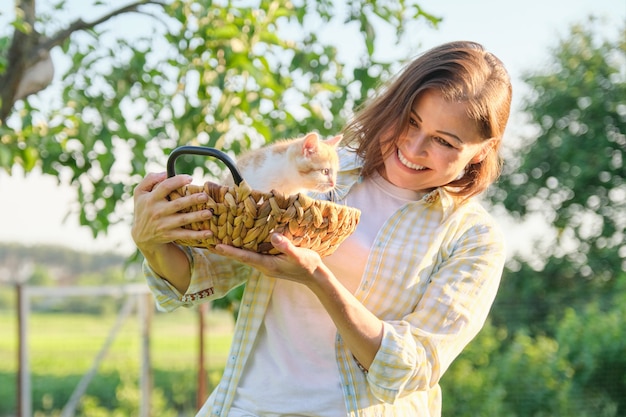 Rijpe lachende gelukkige vrouw met gember kitten in mand