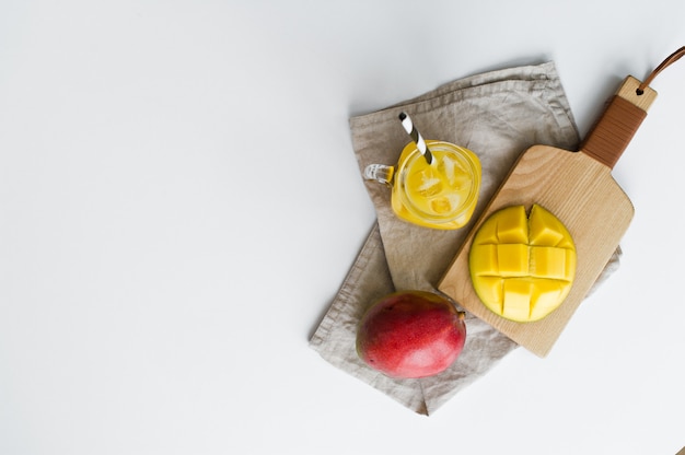 Rijpe mango, halve mango en een glas mangosap met een buis op een houten snijplank.