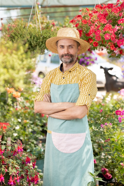 Rijpe mannelijke landbouwer of tuinman in schort en hoed die zich in serre tussen bloembedden en ingemaakte bloemen bevinden