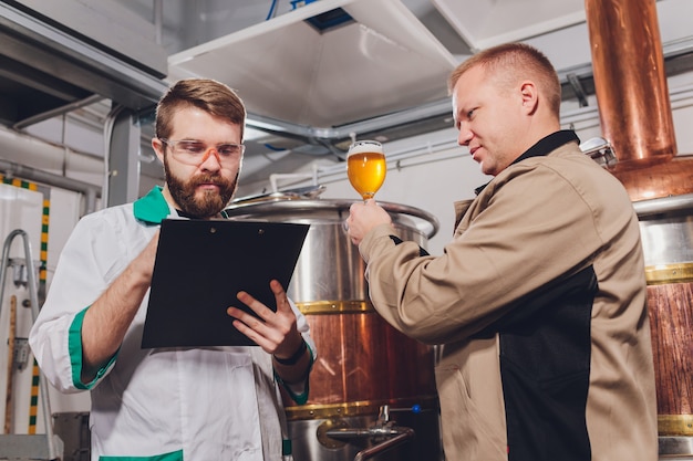 Rijpe mens die de kwaliteit van ambachtbier onderzoekt bij brouwerij. Inspecteur die bij alcohol productiefabriek werkt die bier controleert. Mens die in distilleerderij kwaliteitscontrole van bier van het vat controleert.