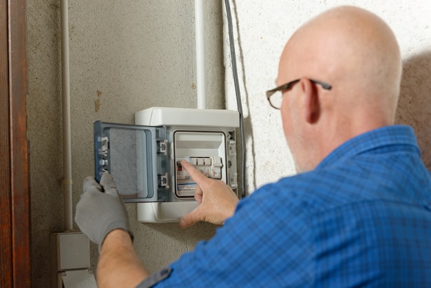 Rijpe mens die met elektrische doos bij huis werkt