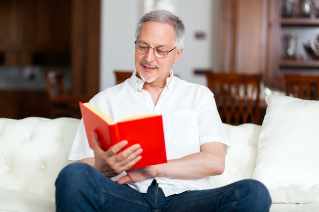 Rijpe mens die terwijl thuis het lezen van een boek op een bank ontspant