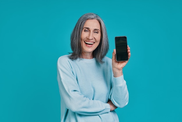 Rijpe mooie vrouw die haar slimme telefoon toont en glimlacht