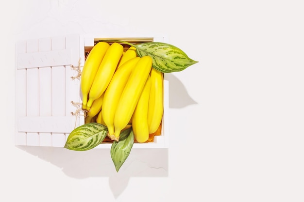 Rijpe natuurlijke bananen met bladeren in een witte houten kist