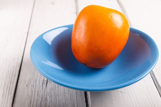 Rijpe oranje dadelpruim in een blauwe plaat op witte houten achtergrond