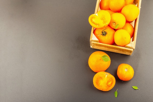 Rijpe oranje tomaten met verse basilicum. Nieuwe oogstgroenten in een houten krat. Zwarte stenen betonnen achtergrond, bovenaanzicht