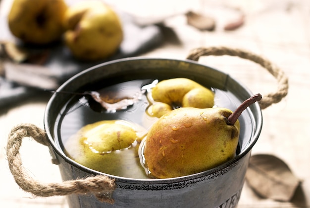 Rijpe peren en perenbladeren in een ijzeren emmer met water en op een houten tafel. Rustieke stijl.