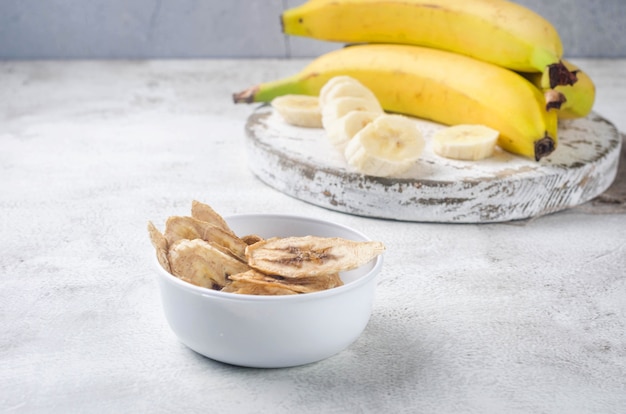 Foto rijpe rauwe banaan en gedroogde bananenschijfjes chips in plaat op lichtgrijze achtergrond. fruitchips. gezond eetconcept, snack, geen suiker. bovenaanzicht, kopieer ruimte.