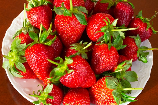 Rijpe rode aardbeien in een witte plaat op een houten tafel, zomer, juli, dessert