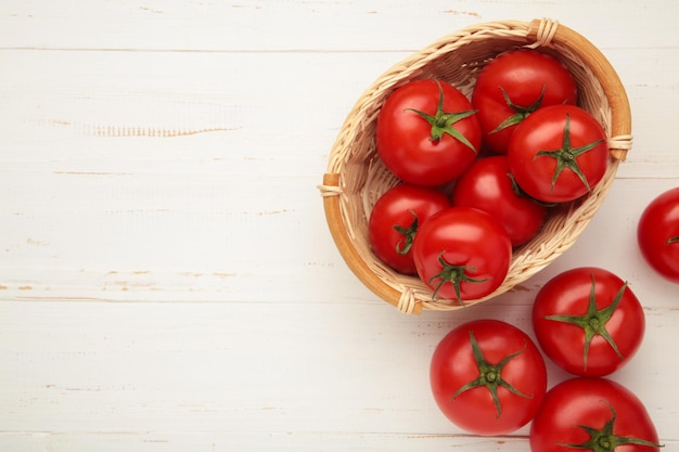 Rijpe rode tomaten in een mand op witte houten achtergrond