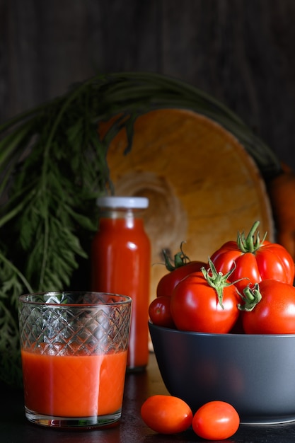 Foto rijpe rode tomaten in kom, tomatensap in glas op donkere achtergrond. verticaal