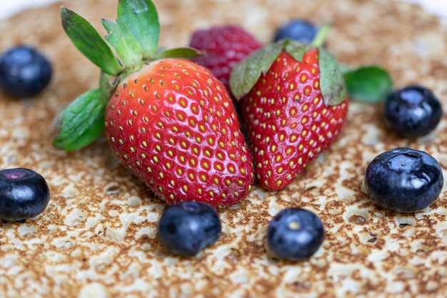 Rijpe sappige aardbeien en bosbessen liggen op een heerlijke pannenkoek. Russische keuken nationale schotel bliny met verse bessen.