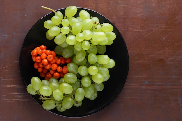 Rijpe, sappige druiven en lijsterbessen op een zwarte plaat op een donkere achtergrond Rauw en biologisch fruit geoogst uit de tuinclose-up