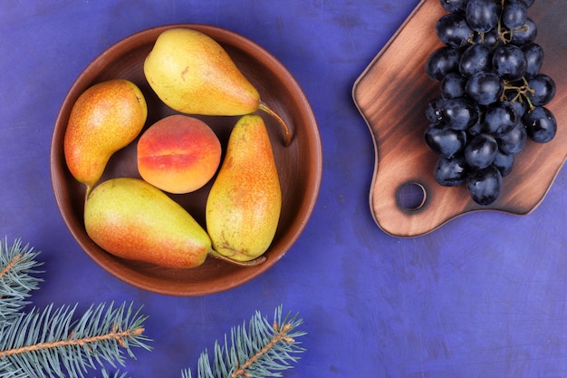 Rijpe sappige peren en perzik in een kleiplaat op een blauwe achtergrond Fruit in een bord en donkere druiven op een houten plankclose-up