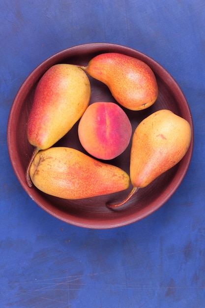 Rijpe sappige peren en perzik in een kleiplaat op een blauwe achtergrond Vers fruit voor veganistische close-up